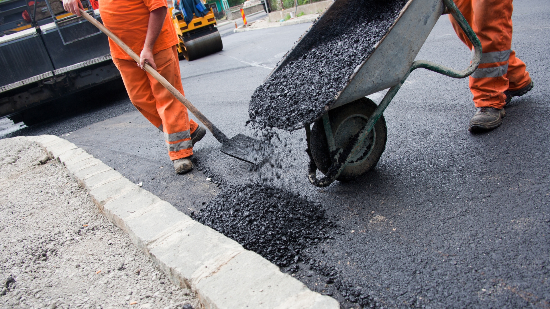 A man with a wheelbarrow pouring cement onto a street